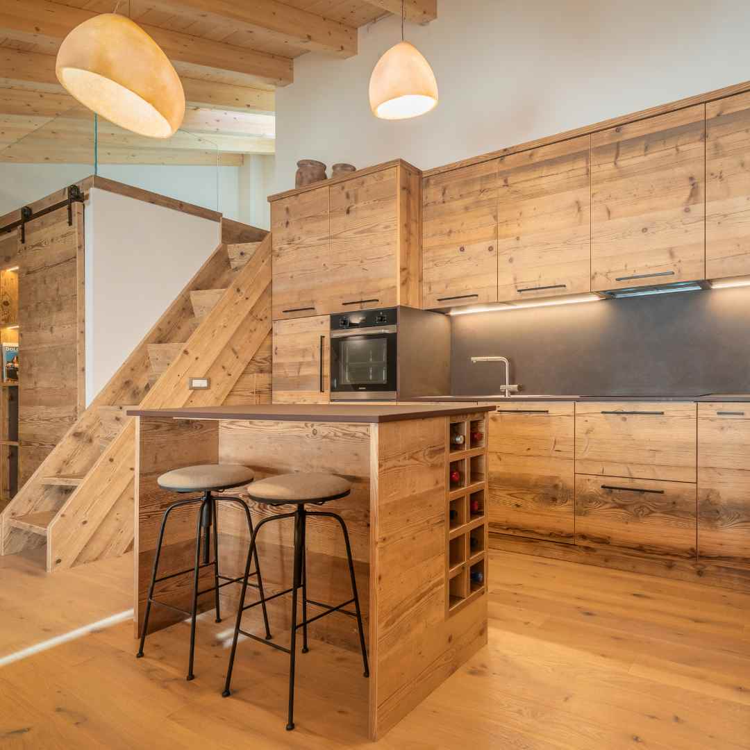 Cucina in legno con isola con vano portabottiglie su misura e sgabelli.